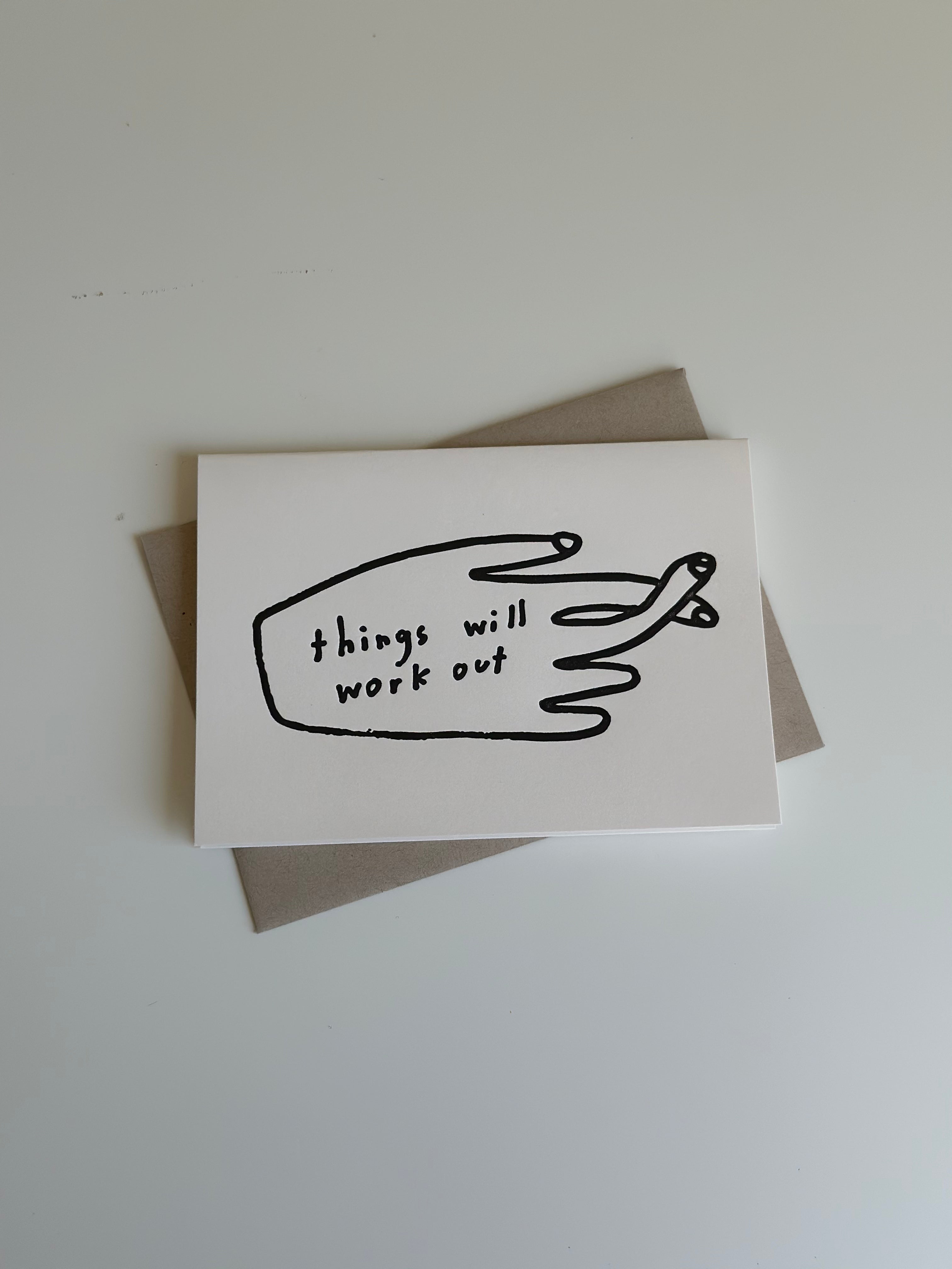 Minimalist encouragement card with simple hand illustration and the phrase ‘Things will work out,’ paired with light beige envelope.