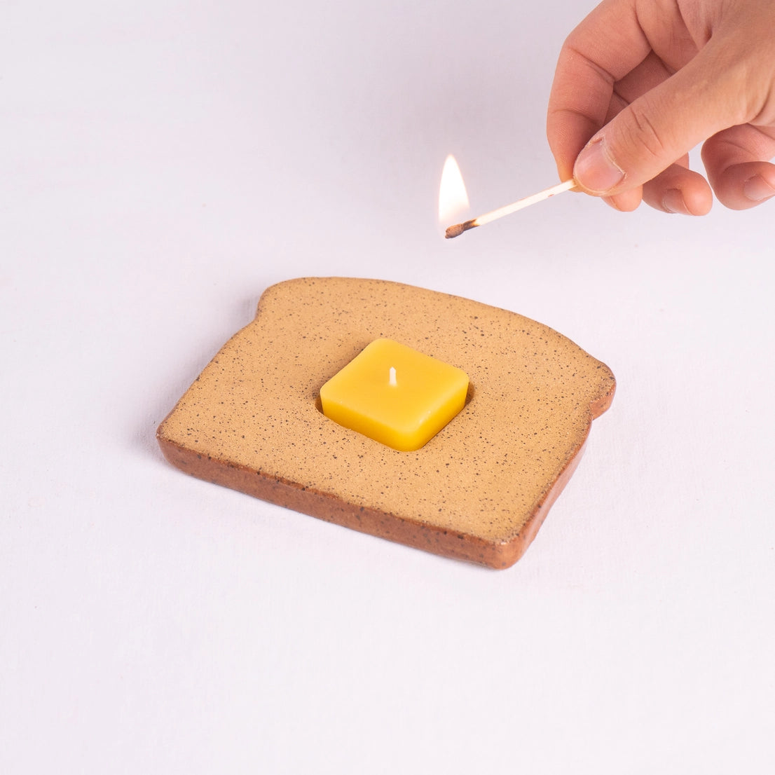 Handmade ceramic toast-shaped candle holder with a beeswax butter tealight being lit