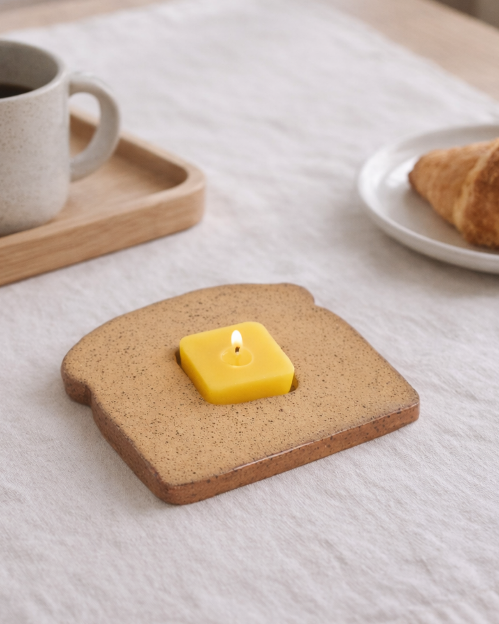 Bread toast candle with butter cube candle beside coffee mug and croissant, whimsical food shaped candle for breakfast table decor.