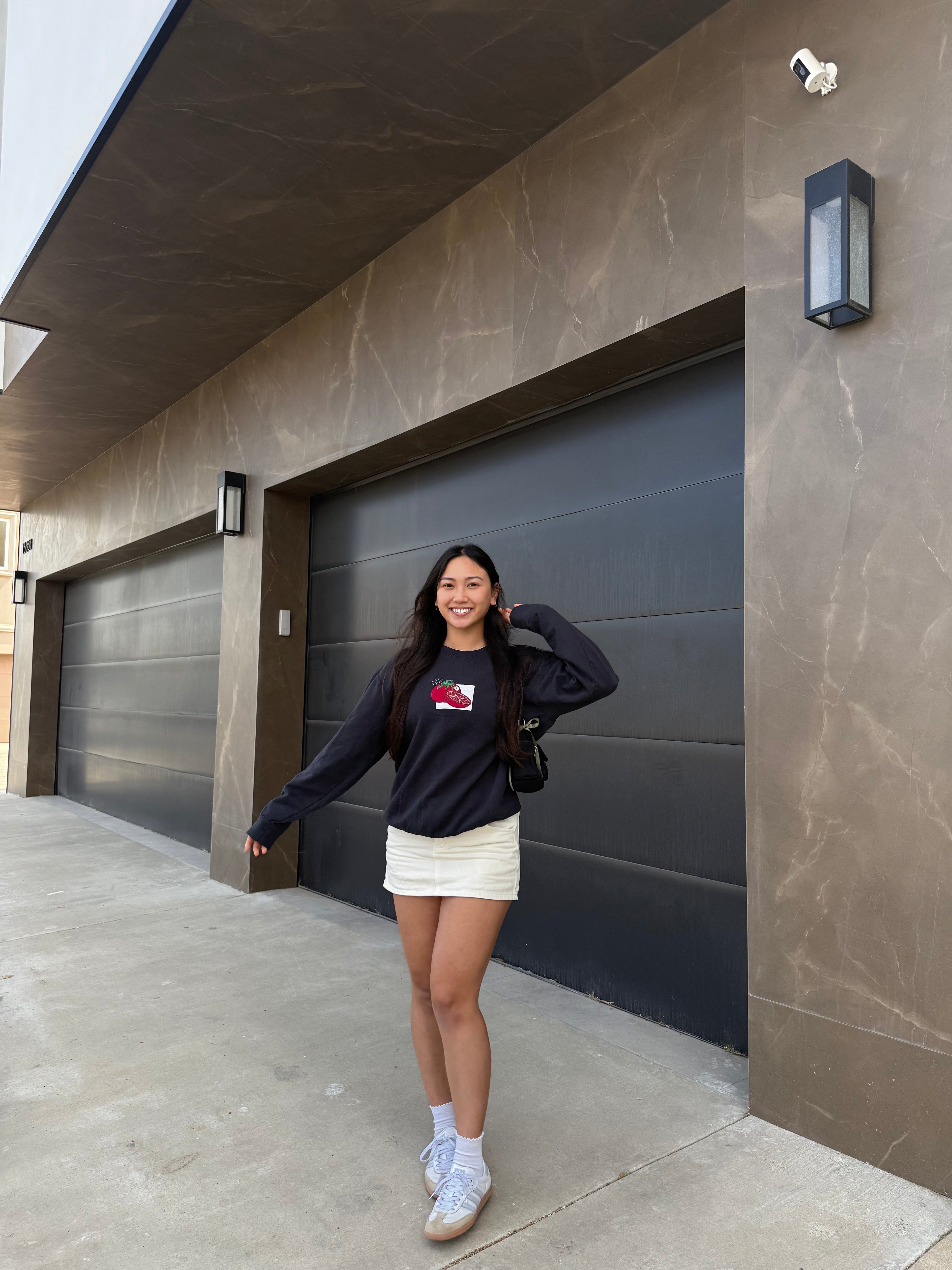 Full-body view of a woman wearing a tomato patchwork embroidered sweatshirt styled with a skirt, cozy design-forward foodie outfit.