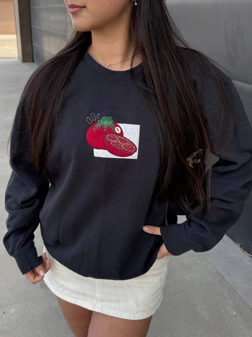 Woman wearing a black tomato embroidered sweatshirt styled casually outdoors, relaxed fit foodie crewneck with playful design.