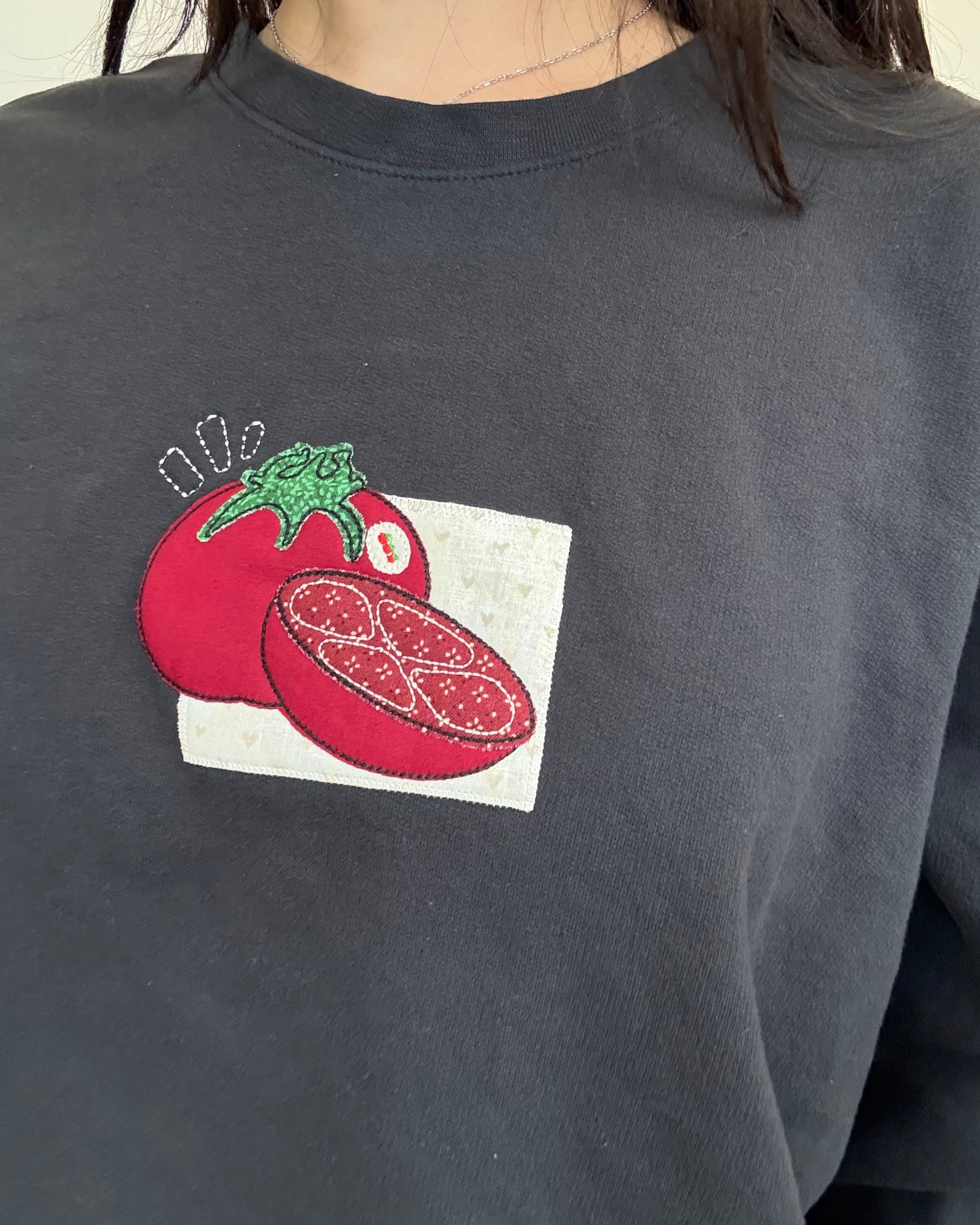Close-up of red tomato patchwork embroidery stitched onto vintage black sweatshirt, showing handmade texture and detailed stitching.