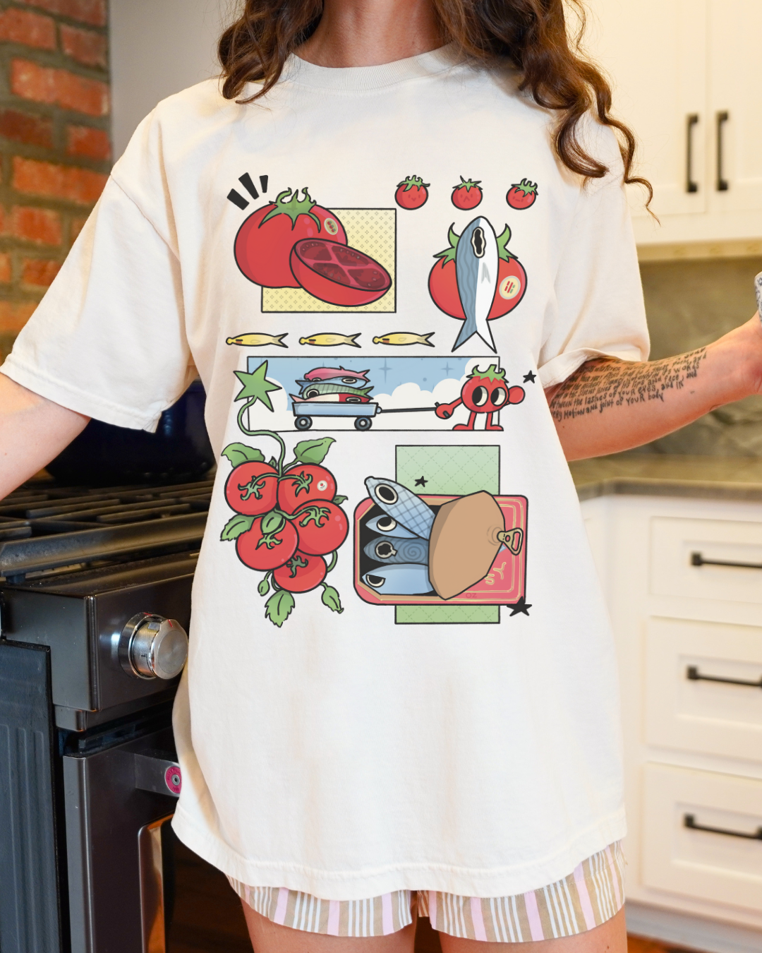Person wearing an ivory tomatoes and sardines graphic t-shirt styled casually indoors near a kitchen