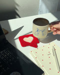Red tufted heart mug rug coaster under coffee mug, placed on a white desk with cozy decor

