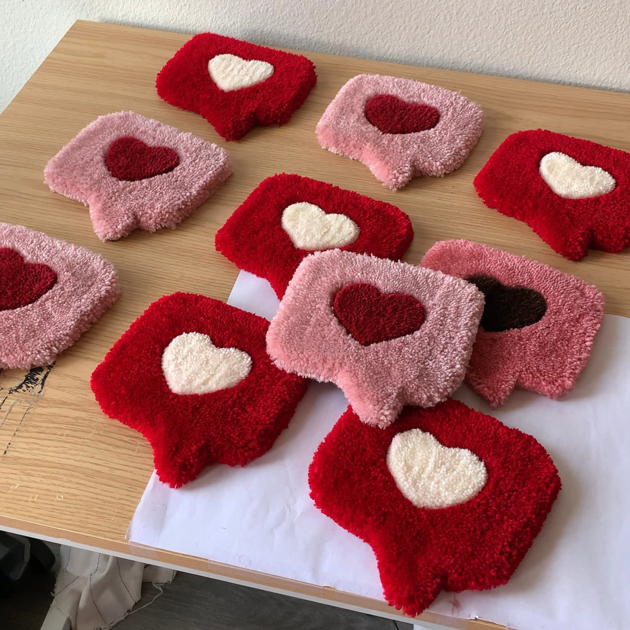 Multiple handmade tufted heart mug rugs in red and pink arranged on a table, plush coaster decor ideal for Valentine’s gifts and cozy spaces.
