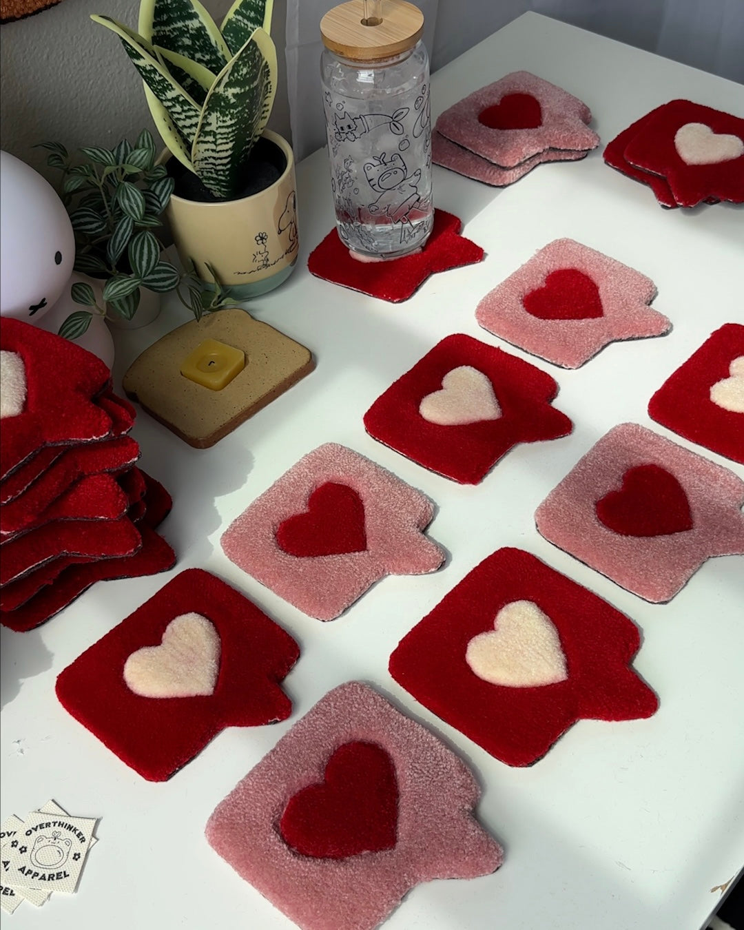 Handmade tufted heart coasters laid out in red and pink colorways, styled for dorm or gifting