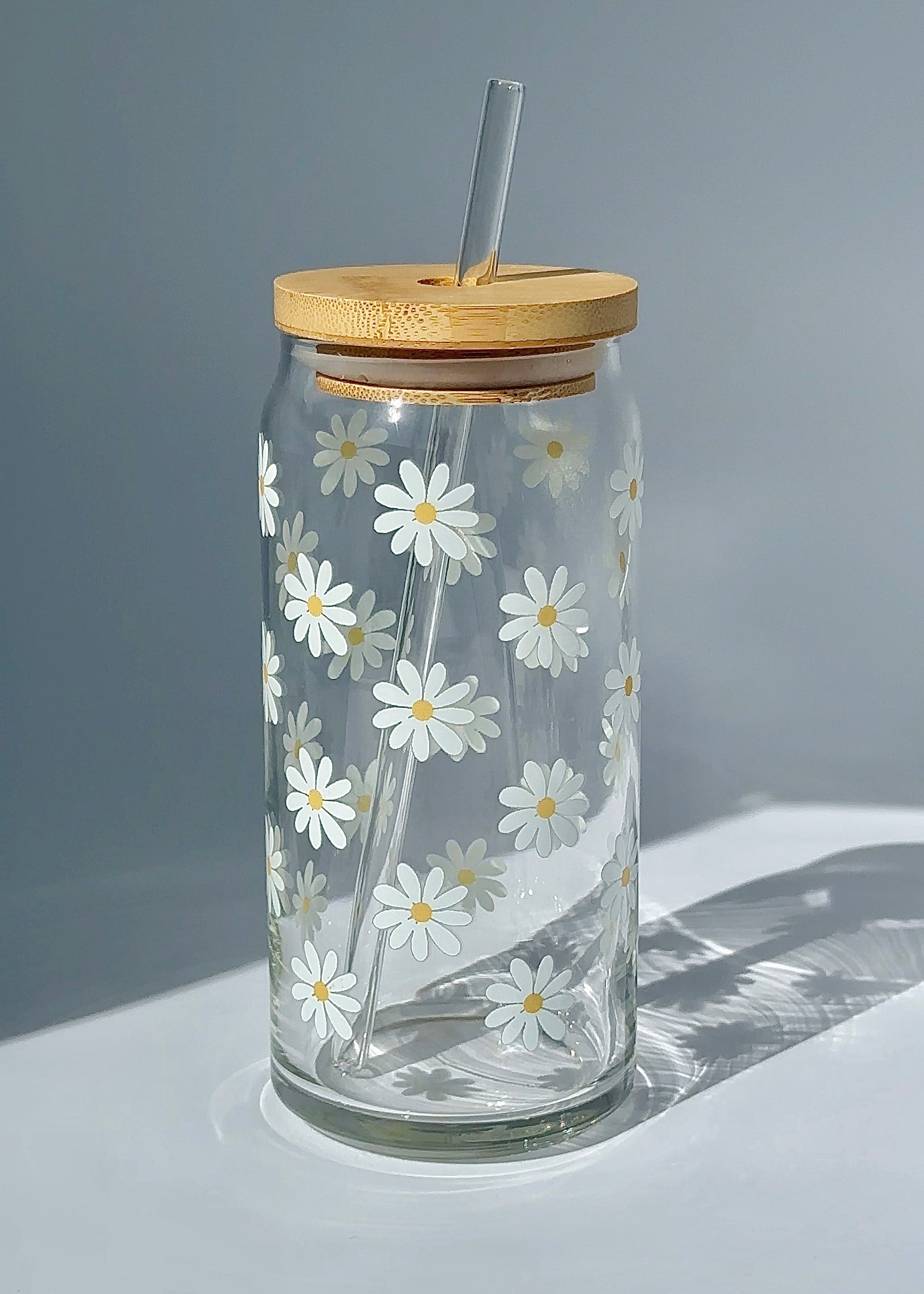 20 oz white daisy glass can with a bamboo lid and reusable glass straw, featuring a simple repeating floral design.
