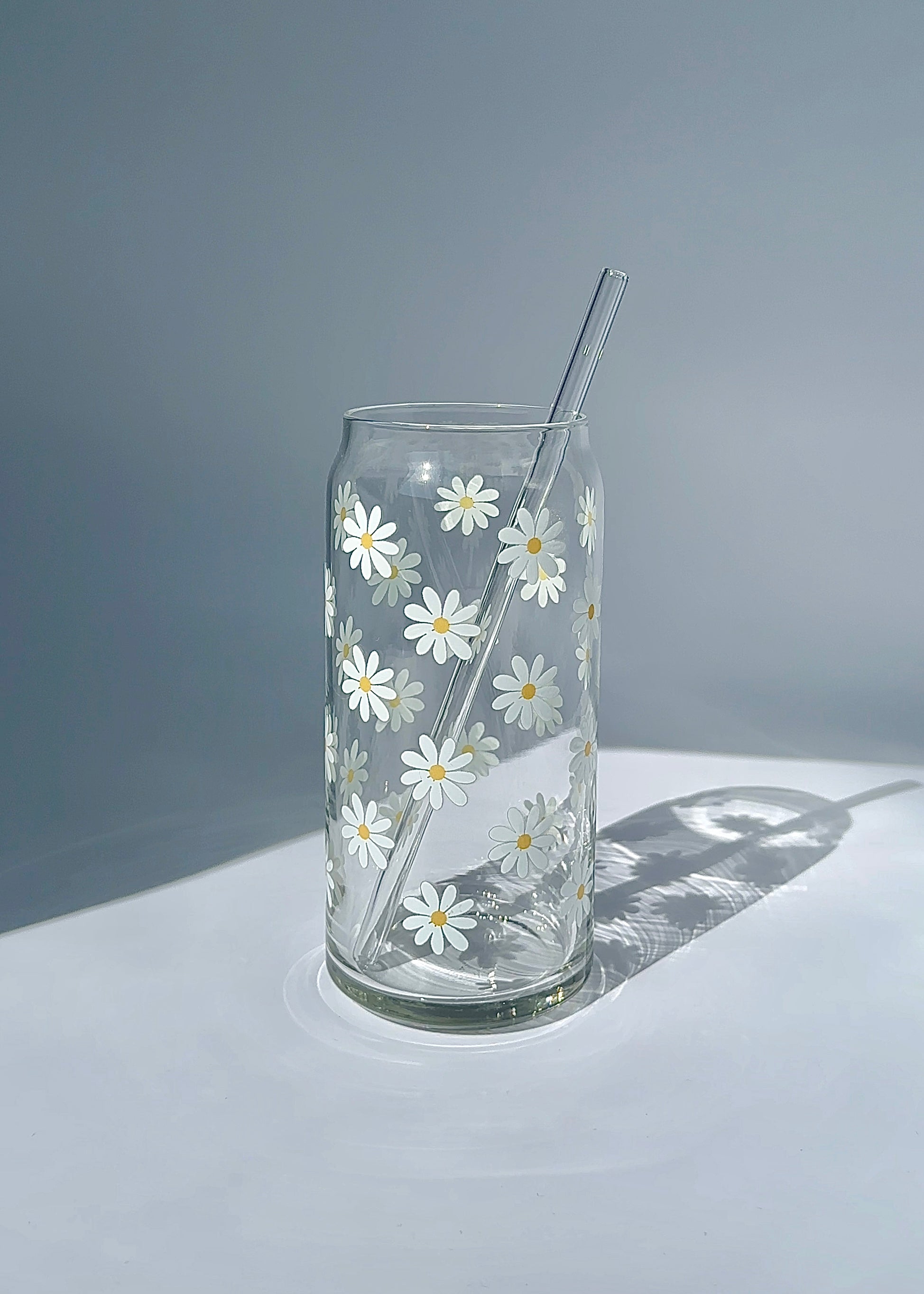 Minimalist 20 oz white daisy glass can with a reusable glass straw, shown empty in bright natural light.