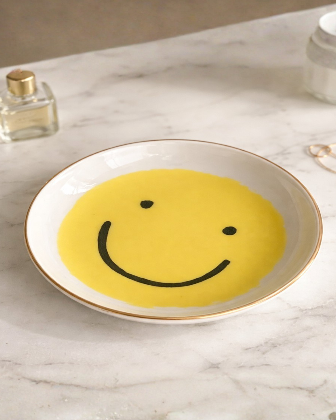 Yellow smiley face ring holder dish on marble vanity surface with perfume bottle and gold jewelry, cute jewelry organizer tray